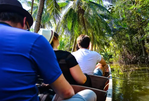 Tourists riding a wooden boat through palm-lined canals near Bangkok