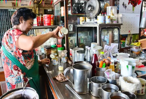 Local Thai coffee vendor pouring condensed milk into glass cups at a traditional café setup