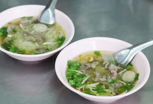 Authentic Thai beef noodle soup served in pink bowls at a traditional Bangkok eatery