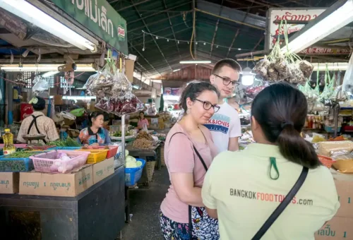 Bangkok Food Tours guide explaining spices and herbs to tourists at a traditional Thonburi market