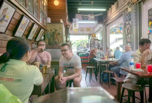 Tourists enjoying drinks and conversation inside a vintage Thai café with wooden décor