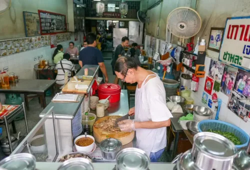 Thai street food chef preparing meat at a traditional open-kitchen restaurant in Thonburi