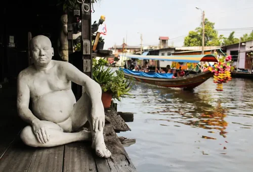 Artistic sculpture sitting along a Thonburi canal with a passing longtail boat in the background