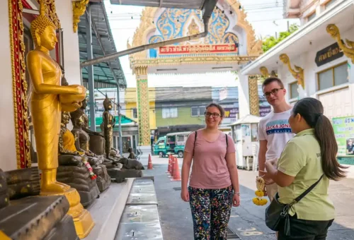 Travelers visiting a Buddhist temple in Thonburi, viewing golden statues and learning cultural stories