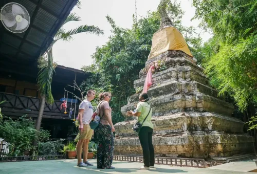 Tour guide explaining the history of a hidden ancient stupa to curious travelers in Thonburi