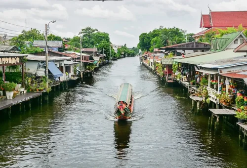 Traditional longtail boat cruising down a calm Bangkok canal lined with riverside homes and shops