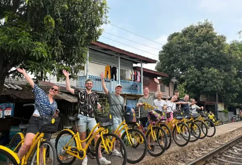 Tour group raising hands on bikes by Bangkok train track