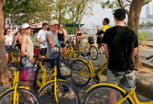 Cyclists riding across a small wooden bridge in a green area of Bangkok