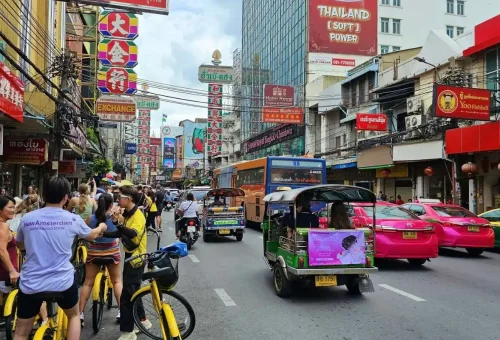 Smiling woman poses on a bridge with the Chao Phraya River and colorful buildings in background.