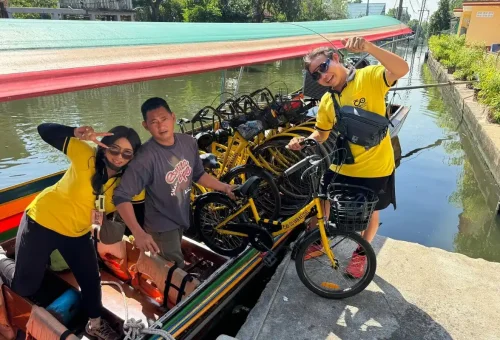 Tourists cycling along a narrow path beside banana trees in rural Bangkok.