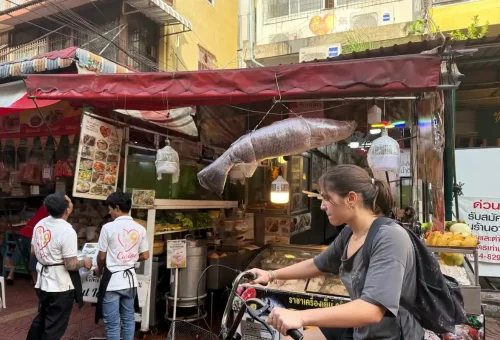 Cyclists exploring the bustling streets of Bangkok’s Chinatown filled with colorful signs, street life, and historic energy.