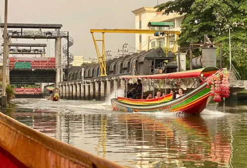 Colorful longtail boat cruising Bangkok canal with tourists, part of the full-day bicycle and boat tour experience.