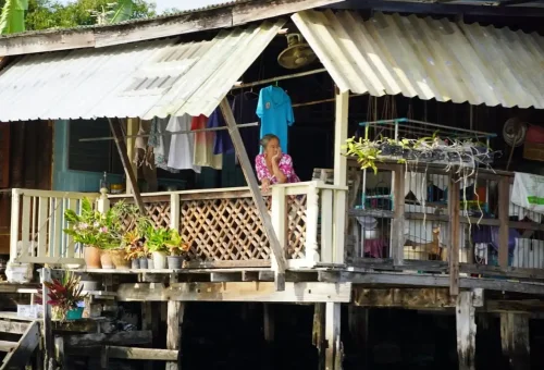 Elderly woman sitting on porch of stilt house over canal
