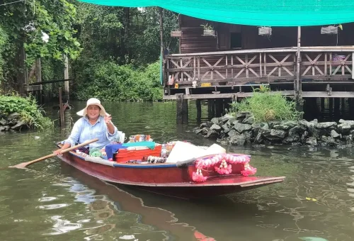Thai woman paddling floating shop in wooden boat
