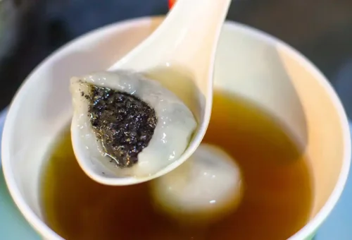 Sesame dumpling in ginger tea held on a spoon over hot syrup