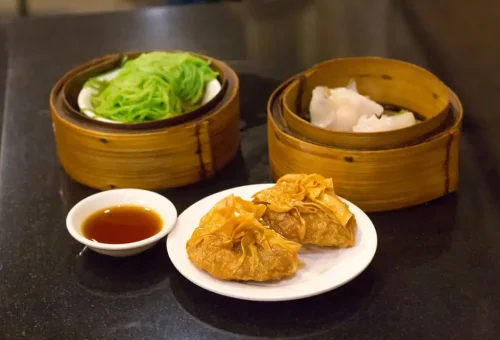 Dim sum, green noodles, and dipping sauce on a table during Bangkok food tour