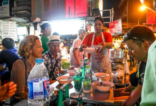 Tourists enjoying local soup at a night market table in Bangkok Chinatown