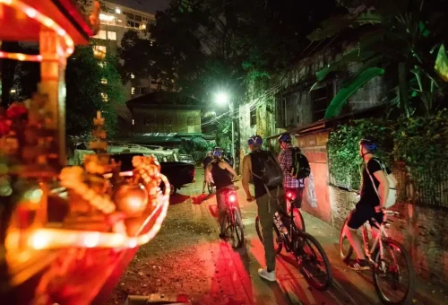 Our group bikes past Bangkok’s forgotten homes and spirit houses, glowing in soft red light.