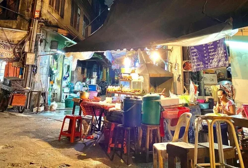 Friendly vendor prepares grilled skewers — authentic late-night bites in Bangkok’s hidden markets.