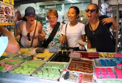 Tourists enjoying Thai street desserts at a Bangkok market