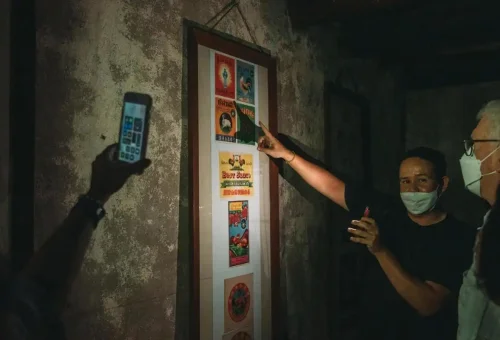 Guide pointing at framed historic product labels in dimly lit home