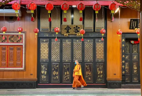 Monk walking past Chinese temple adorned with lanterns