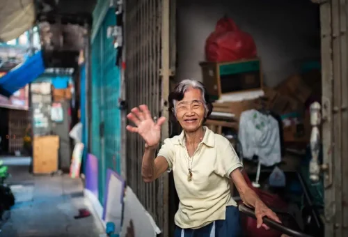 Elderly woman waving and smiling in front of her home in Bangkok