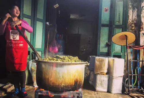 Woman cooking traditional greens over open fire in Chinatown Bangkok