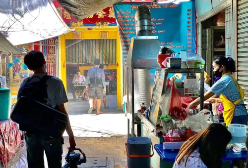 Food vendor preparing dishes beside a shrine in Chinatown Bangkok