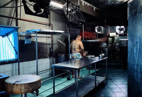 Butcher in traditional Bangkok kitchen with hanging roast meats