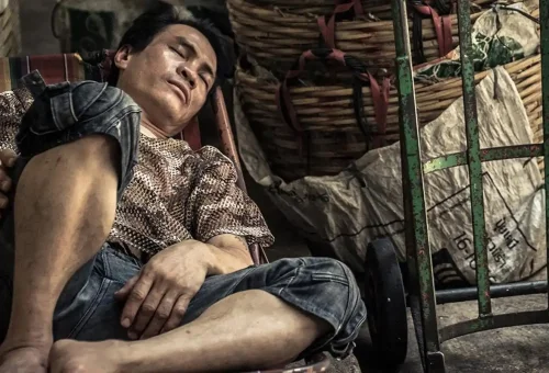 Local man sleeping beside woven baskets in a Chinatown alley