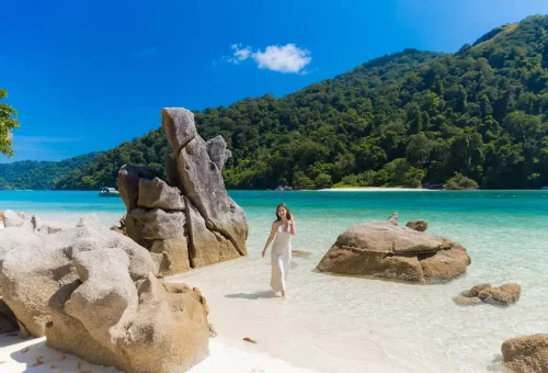 Woman walking in shallow sea next to rock formations on Surin Islands