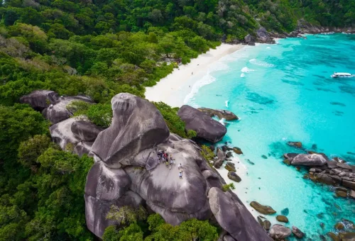 Tourists standing atop Sail Rock with panoramic views of white sand beaches and turquoise bays at Similan Islands.