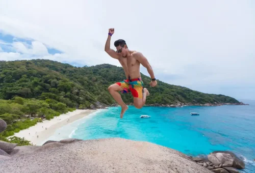 Tourist jumping for joy on a cliff viewpoint above Similan Islands beach.