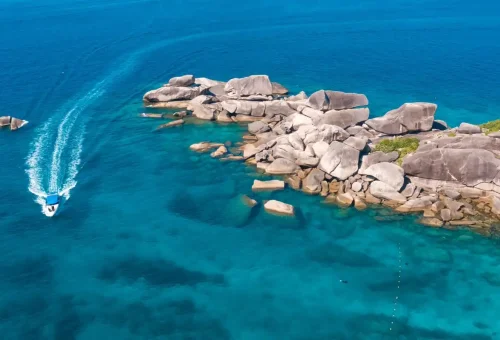 Speedboat cruising over the crystal-clear waters of Similan Islands near rocky coastline.