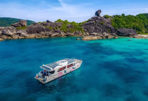 Colorful speed catamaran floating in turquoise water near Sail Rock at Similan Islands with tourists sunbathing and hiking the iconic viewpoint.