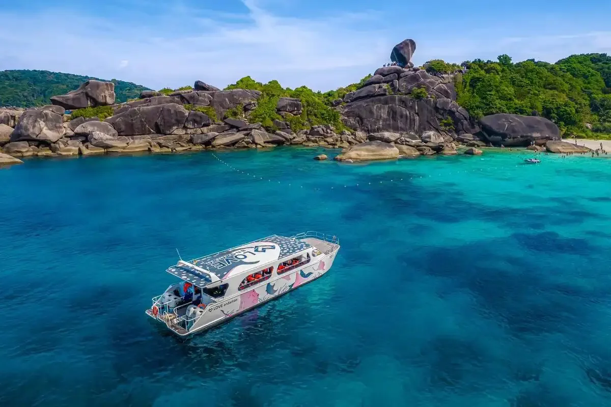 Colorful speed catamaran floating in turquoise water near Sail Rock at Similan Islands with tourists sunbathing and hiking the iconic viewpoint.