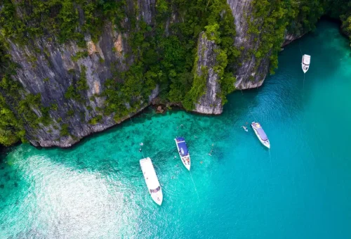 Speedboats anchored near towering cliffs and emerald water at Pileh Lagoon.
