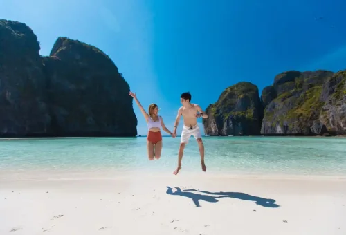 Couple jumping joyfully on Maya Bay’s beach during a Phi Phi tour.