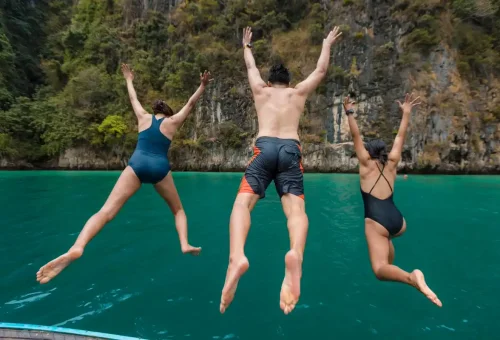 Three tourists jumping off a boat into emerald-green water at Phi Phi.