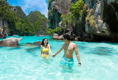 Couple holding hands in shallow water surrounded by cliffs at Phi Phi Islands.