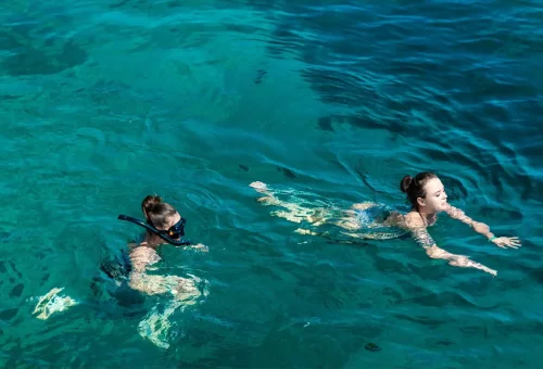 Two women snorkeling and swimming in crystal-clear water.