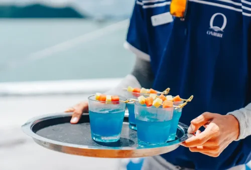 Signature blue welcome cocktails with fruit garnish served by crew on luxury yacht.
