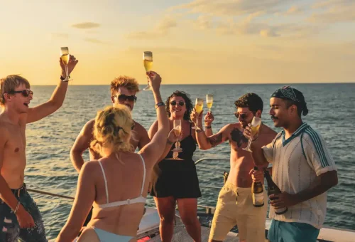 Happy travelers raising champagne glasses on deck at sunset during catamaran cruise.