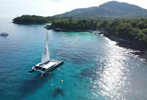 Aerial view of Ombre Catamaran anchored near Racha Island with people swimming around.