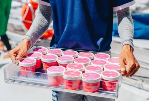 Crew member serving assorted ice cream cups on luxury yacht during island tour.