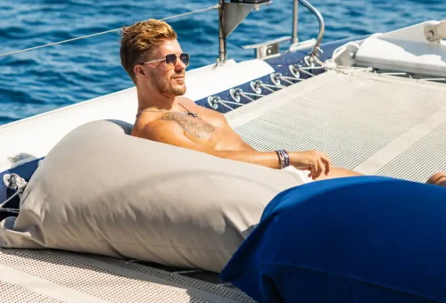 Man relaxing on beanbag on netted lounge area of Ombre catamaran