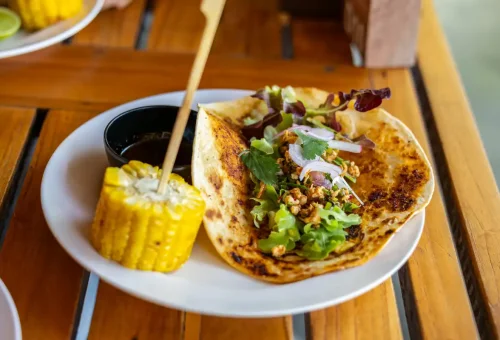 Grilled tortilla wrap with fresh greens, corn on the cob, and dipping sauce