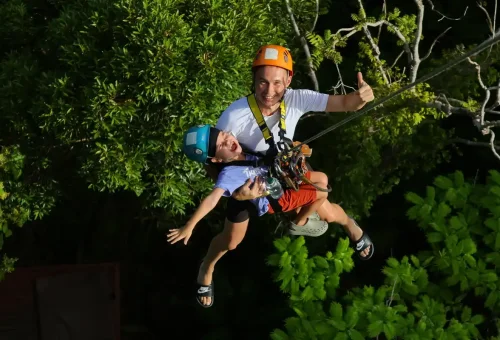 A parent and child enjoying a tandem zipline ride through the lush jungle canopy in Phuket.