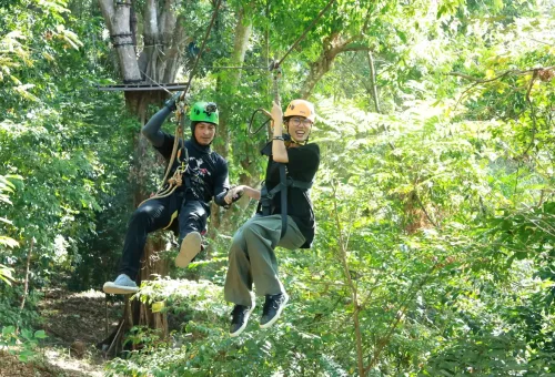 A smiling tourist with a guide mid-zipline through tropical forest at Flying Hanuman, Phuket.